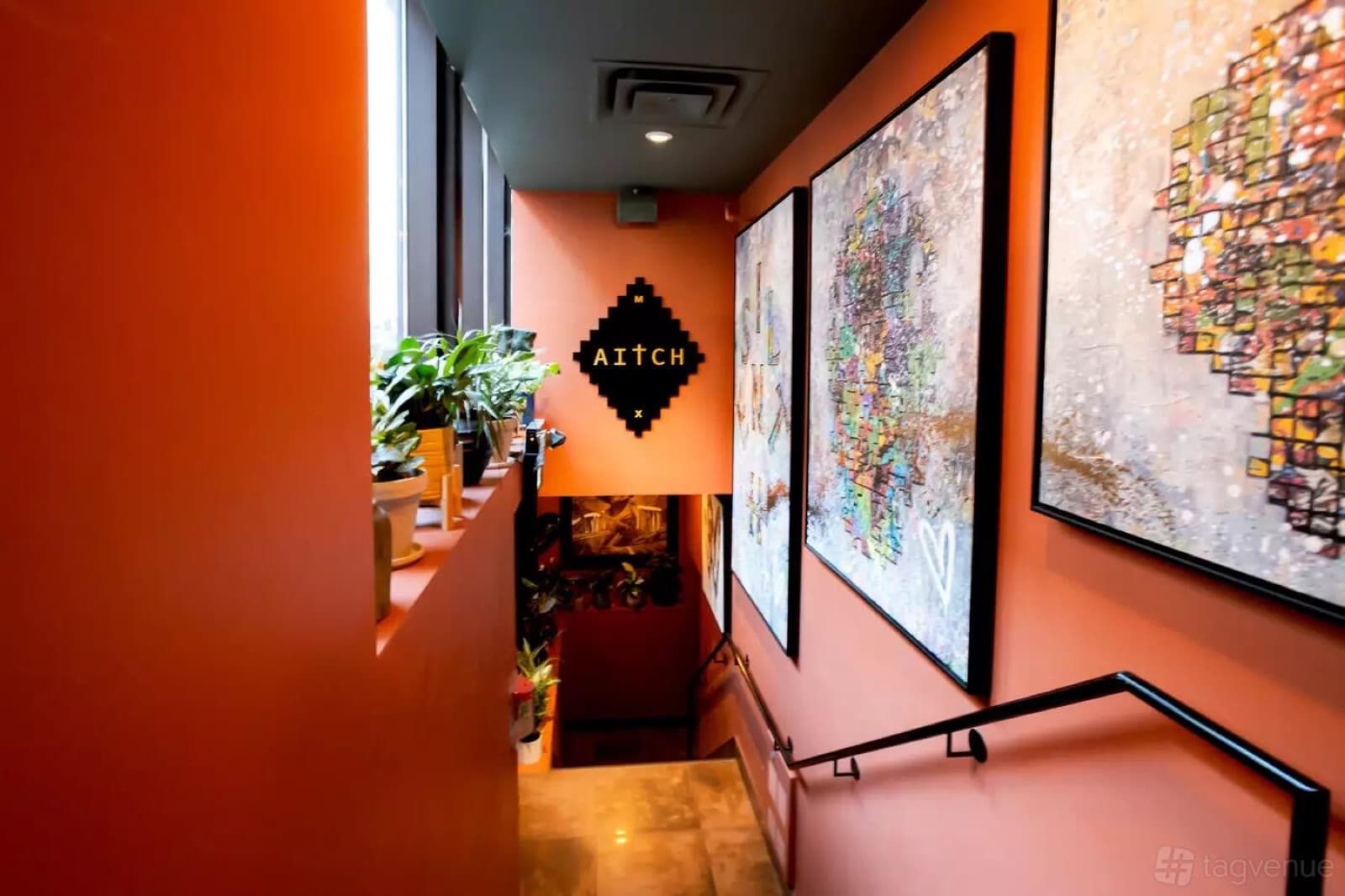 The stairs down to Aitch, past large mosaic artworks on an orange wall