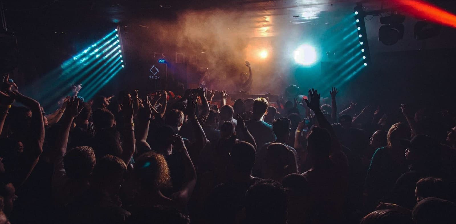 A crowd with hands up under smoky stage lights at Nest