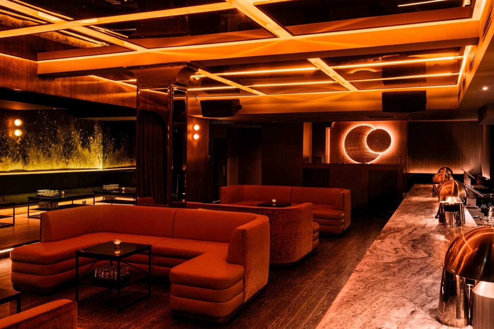 Parc Ave's lounge: orange velvet booths, a glowing ring light and a long gold-lit wall