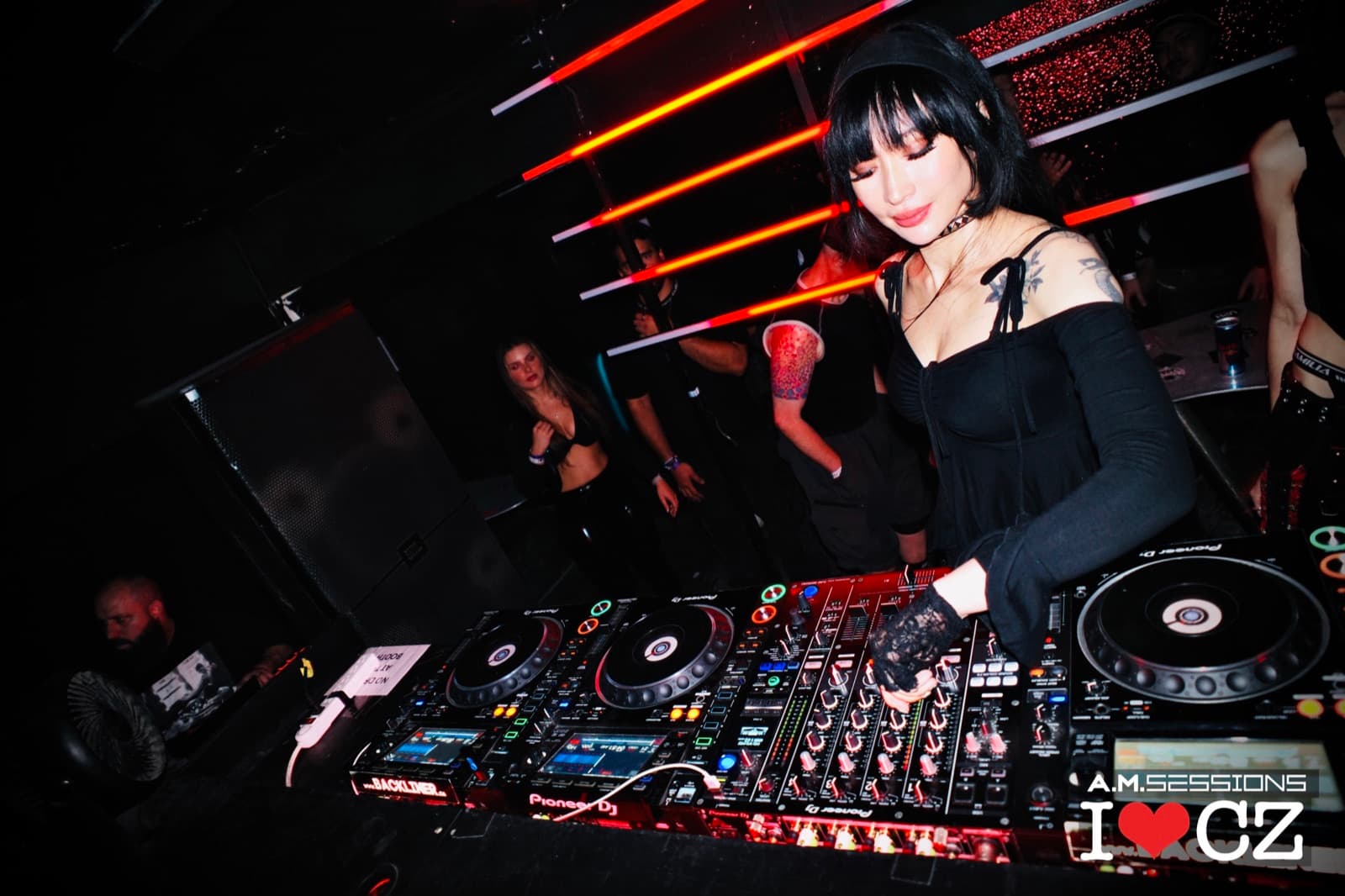 A DJ at the booth beneath red striped wall lights at The Comfort Zone
